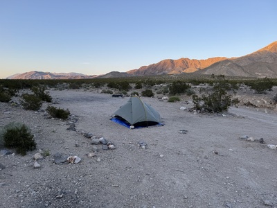 My tent in front of mountains lit by the setting sun.
